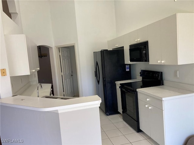 kitchen with a peninsula, a high ceiling, light countertops, black appliances, and white cabinetry