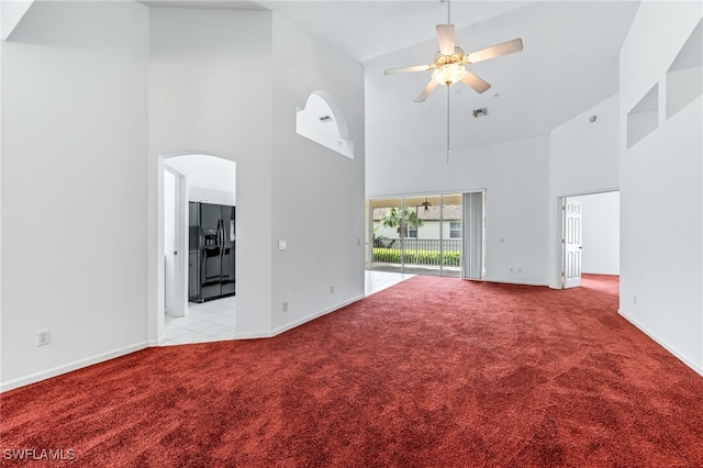 unfurnished living room with baseboards, light carpet, a towering ceiling, arched walkways, and a ceiling fan