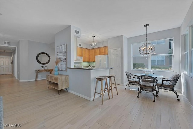 kitchen featuring white appliances, visible vents, hanging light fixtures, an inviting chandelier, and light wood-style floors