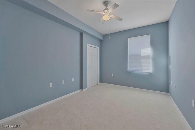 spare room with light carpet, a ceiling fan, and baseboards