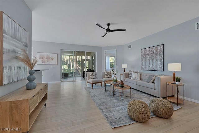 living room with ceiling fan, light wood-type flooring, visible vents, and baseboards