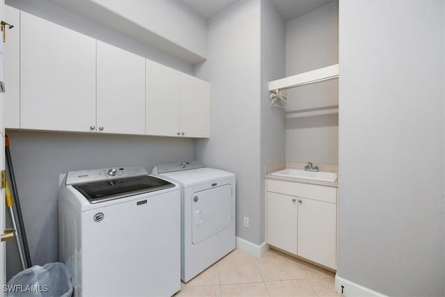 laundry area with light tile patterned floors, separate washer and dryer, a sink, baseboards, and cabinet space