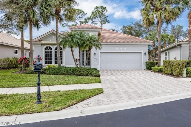 mediterranean / spanish home featuring decorative driveway, a tile roof, stucco siding, a garage, and a front lawn