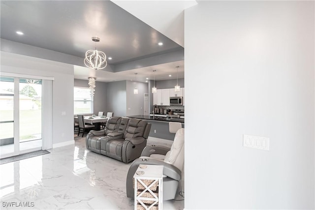 living area with a tray ceiling, marble finish floor, a notable chandelier, and recessed lighting