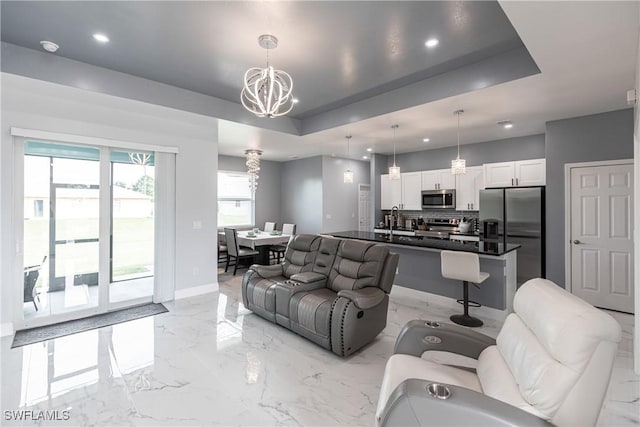 living area with a tray ceiling, marble finish floor, recessed lighting, an inviting chandelier, and baseboards