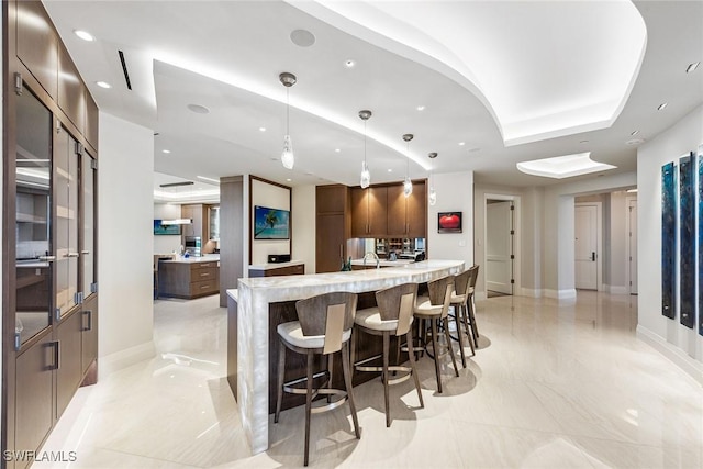 kitchen with a tray ceiling, a breakfast bar area, recessed lighting, and baseboards