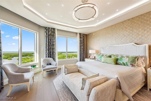 bedroom featuring baseboards, wood-type flooring, a raised ceiling, and wallpapered walls