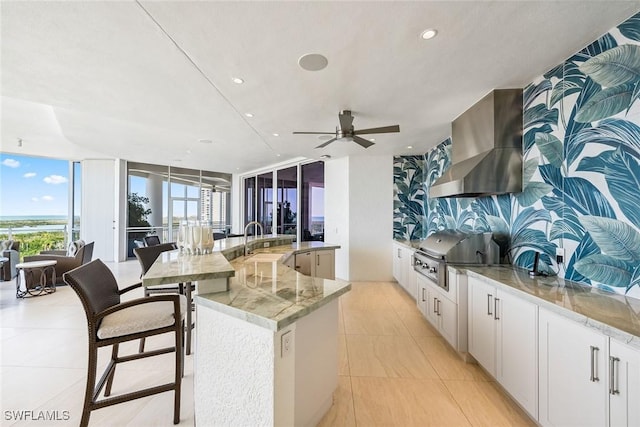 kitchen with wall chimney range hood, a large island, open floor plan, and a sink