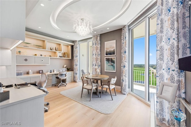 dining space featuring built in desk, light wood finished floors, a chandelier, recessed lighting, and a tray ceiling
