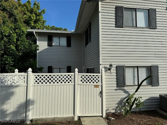 view of property exterior with a gate, fence, and central AC