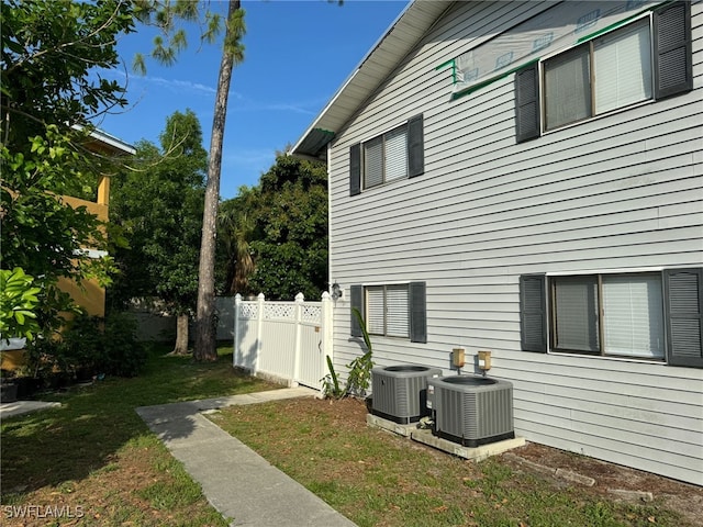 view of side of property with a lawn, fence, and central air condition unit