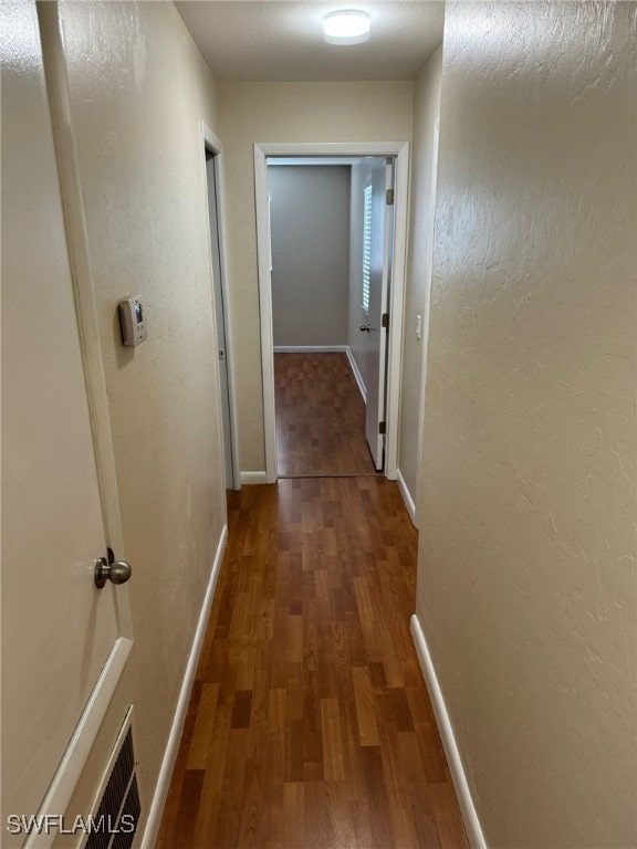 hallway featuring a textured wall, dark wood-style flooring, visible vents, and baseboards