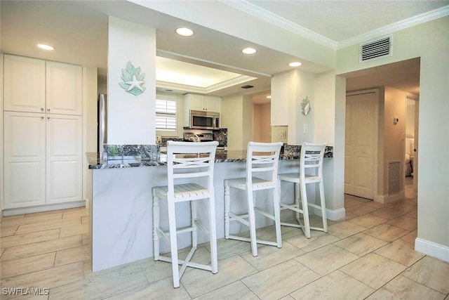 kitchen featuring visible vents, stainless steel microwave, a peninsula, and white cabinetry