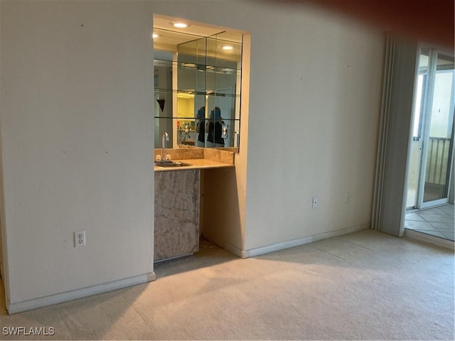 carpeted empty room featuring baseboards, a sink, and wet bar