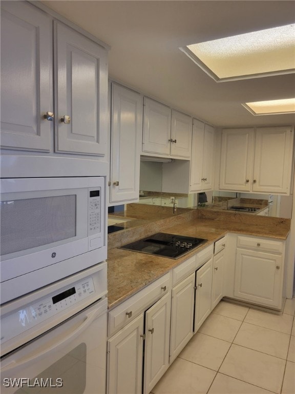 kitchen featuring light stone countertops, white appliances, light tile patterned floors, and white cabinetry