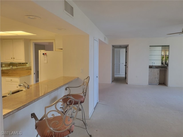 kitchen with light colored carpet, visible vents, freestanding refrigerator, white cabinetry, and a sink