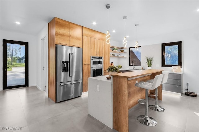 kitchen with pendant lighting, open shelves, stainless steel appliances, light countertops, and a kitchen breakfast bar