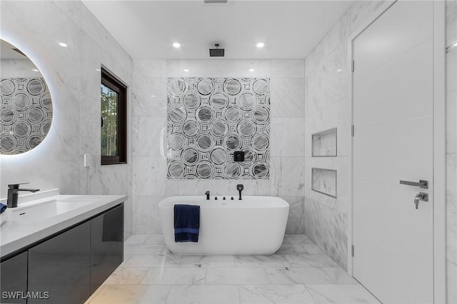 bathroom with marble finish floor, vanity, a freestanding tub, tile walls, and recessed lighting