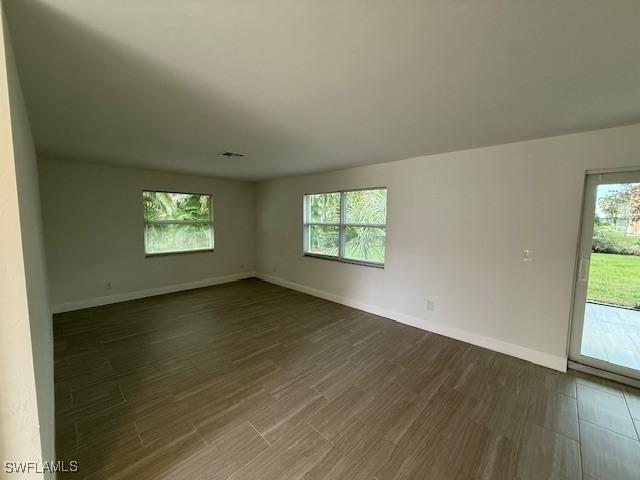 empty room featuring baseboards, dark wood finished floors, visible vents, and a healthy amount of sunlight