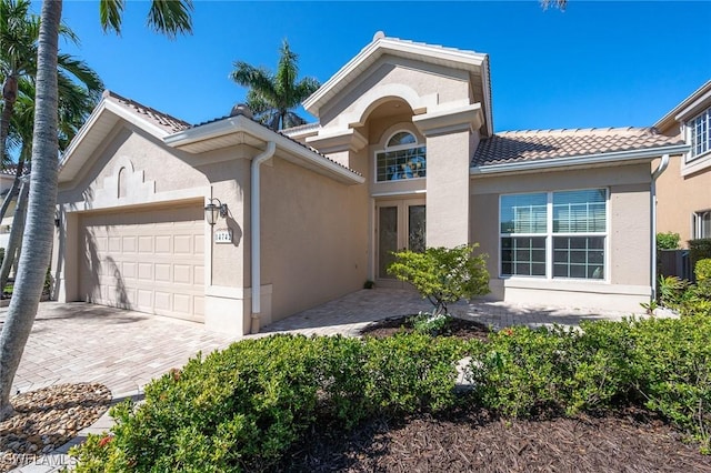 view of front facade featuring a garage, a tiled roof, decorative driveway, and stucco siding