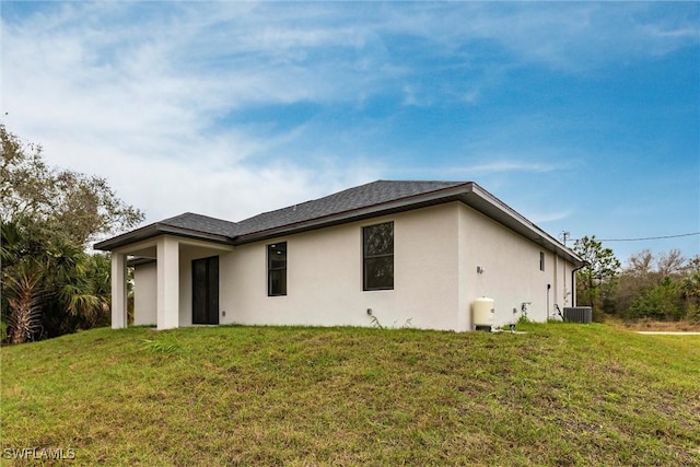 exterior space with stucco siding, a shingled roof, central AC unit, and a yard