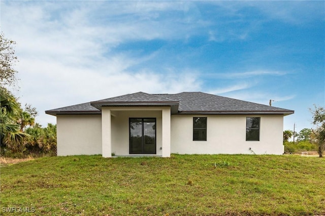 back of house featuring roof with shingles, a yard, and stucco siding