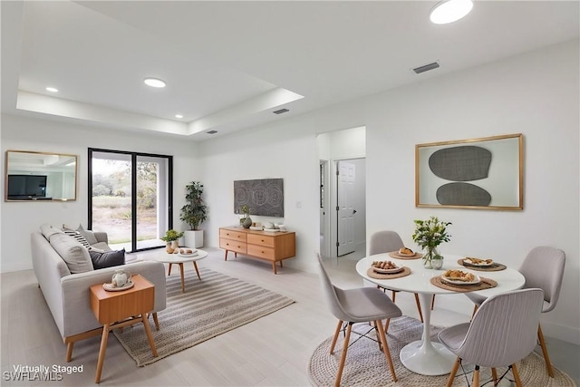 living area with light wood finished floors, visible vents, a tray ceiling, and recessed lighting