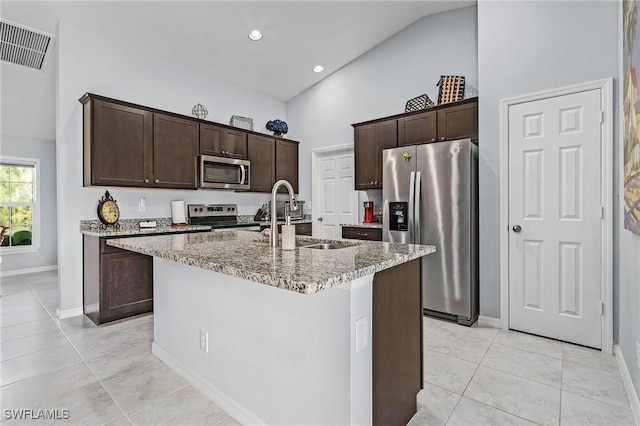 kitchen with stainless steel appliances, visible vents, a kitchen island with sink, dark brown cabinetry, and light stone countertops