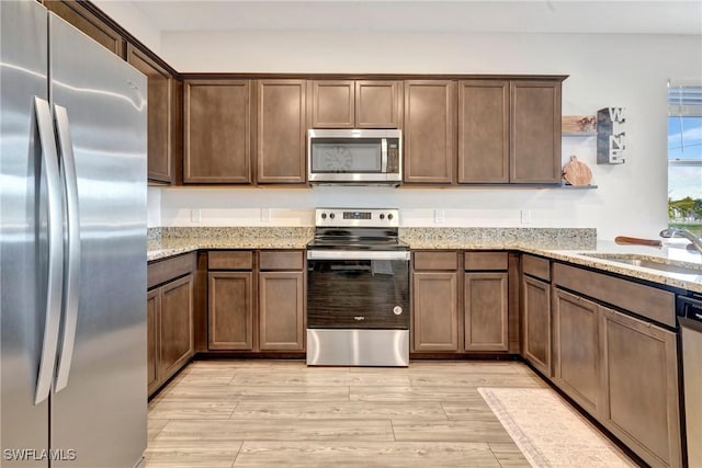 kitchen featuring light stone countertops, appliances with stainless steel finishes, light wood-style floors, and a sink