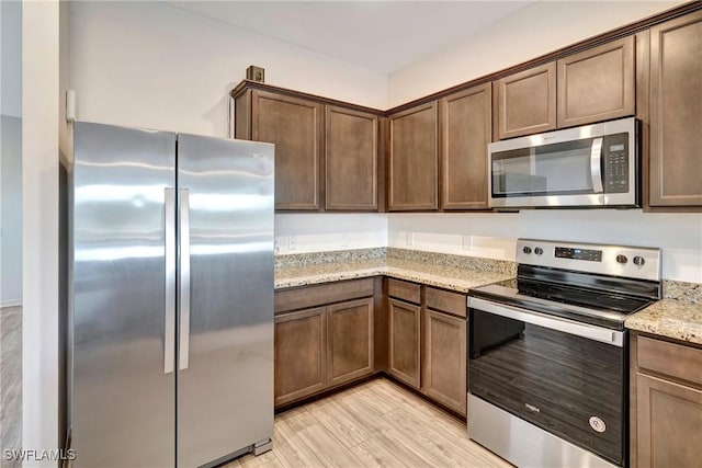 kitchen featuring stainless steel appliances, light wood-style flooring, and light stone countertops