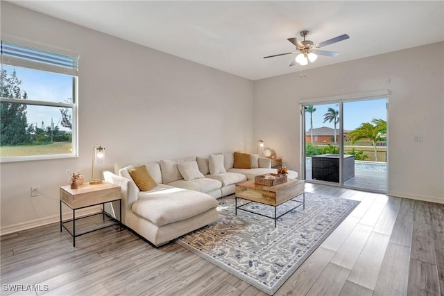 living room with light wood-type flooring, a ceiling fan, and baseboards