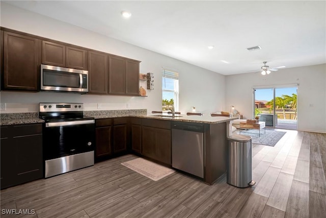 kitchen featuring visible vents, a peninsula, light stone countertops, stainless steel appliances, and a sink