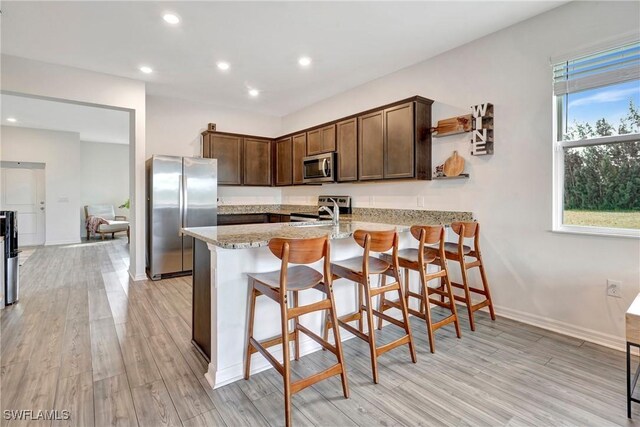 kitchen with a peninsula, appliances with stainless steel finishes, a breakfast bar area, and light stone countertops