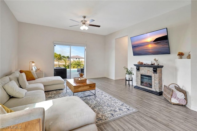 living area with ceiling fan, a fireplace, baseboards, and wood finished floors