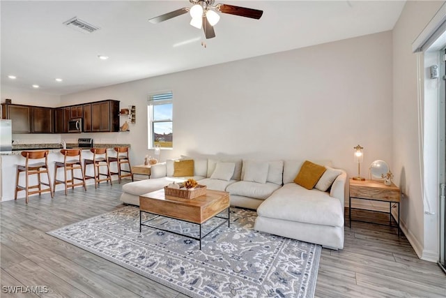 living area featuring light wood-type flooring, ceiling fan, visible vents, and baseboards