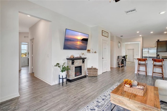 living room featuring a fireplace, recessed lighting, visible vents, light wood-type flooring, and baseboards