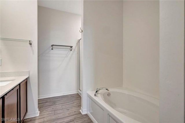 bathroom with a garden tub, wood finished floors, vanity, and baseboards