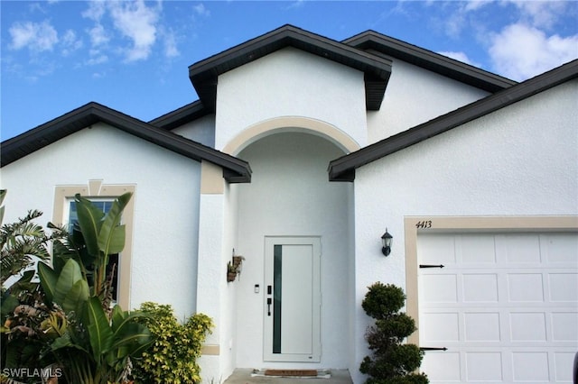 entrance to property with a garage and stucco siding