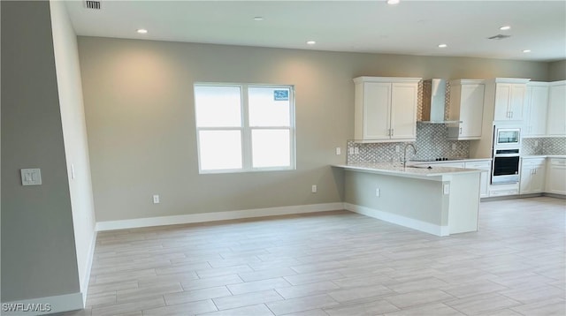 kitchen with white cabinets, wall chimney exhaust hood, appliances with stainless steel finishes, light countertops, and backsplash