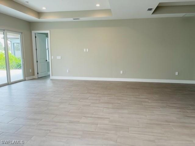 spare room with baseboards, a raised ceiling, and recessed lighting