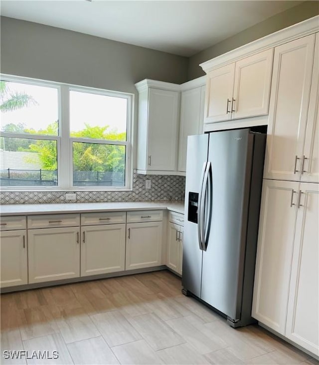 kitchen featuring light countertops, stainless steel fridge, decorative backsplash, and white cabinetry