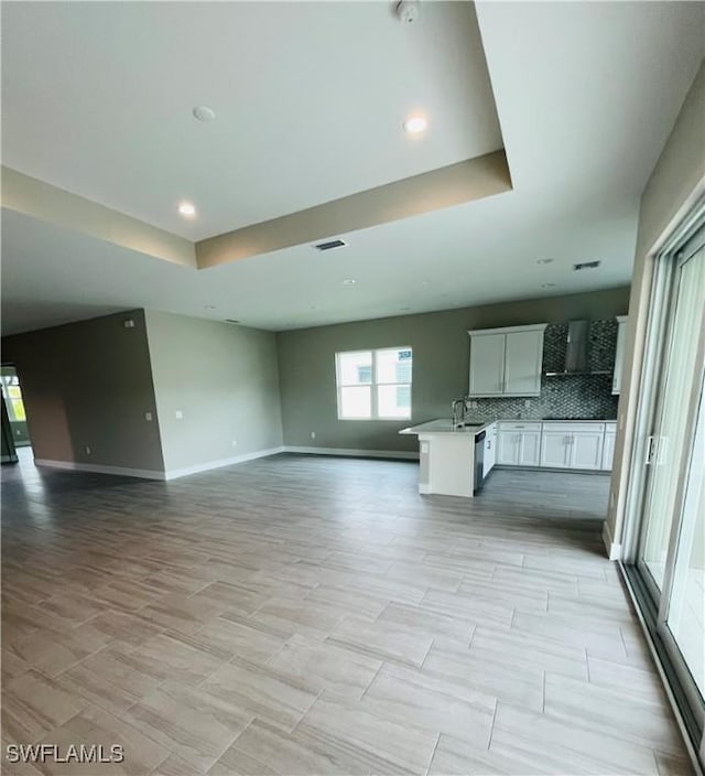 unfurnished living room featuring a sink, recessed lighting, a raised ceiling, and baseboards