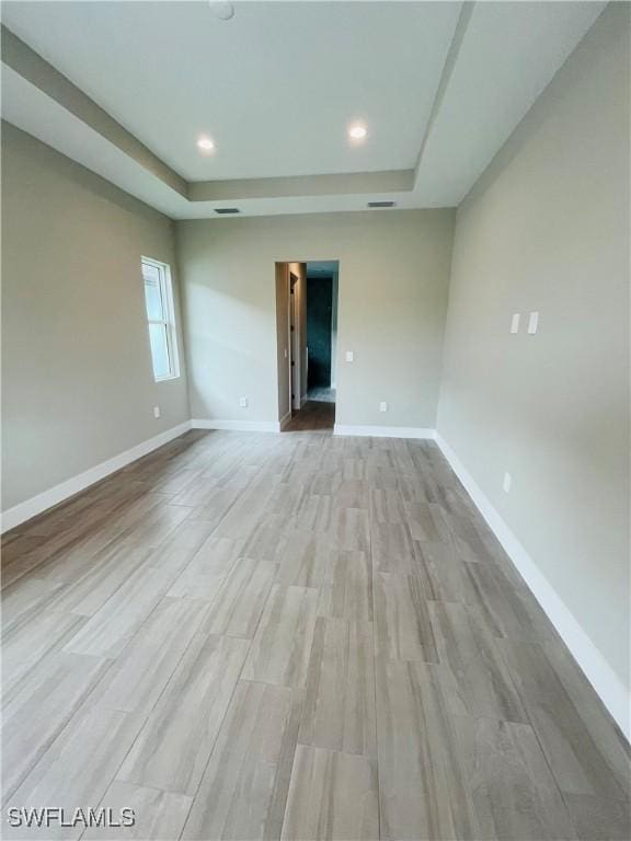 unfurnished room with a tray ceiling, recessed lighting, light wood-style floors, and baseboards