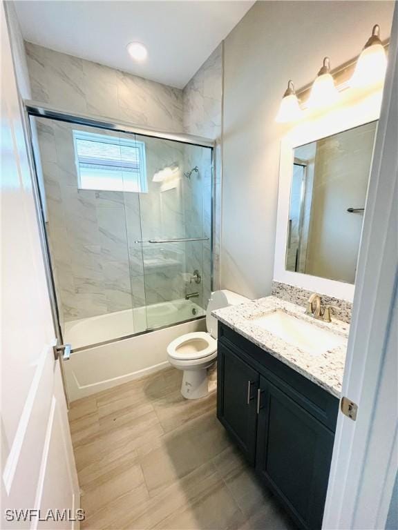 full bathroom featuring toilet, bath / shower combo with glass door, and vanity