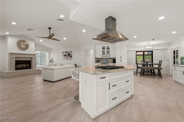 kitchen featuring visible vents, a fireplace with raised hearth, light stone counters, island exhaust hood, and gas cooktop