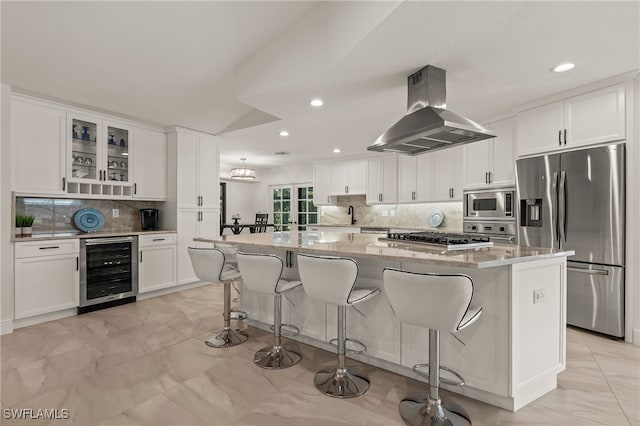 kitchen with island range hood, white cabinets, wine cooler, light stone counters, and stainless steel appliances