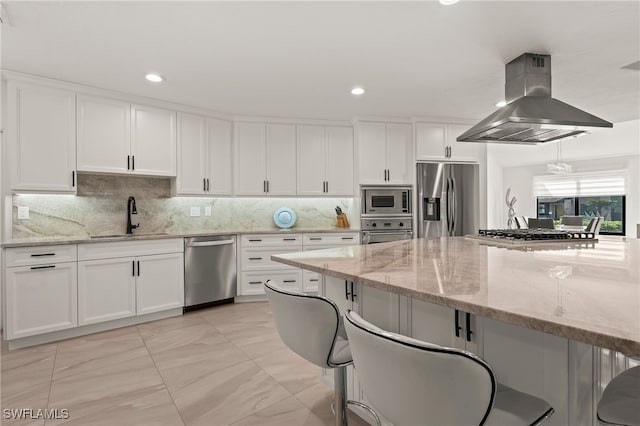 kitchen featuring island range hood, a sink, white cabinetry, appliances with stainless steel finishes, and decorative backsplash