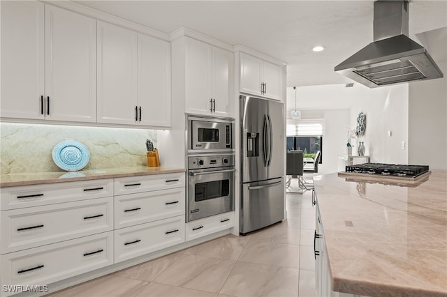 kitchen with white cabinets, appliances with stainless steel finishes, wall chimney range hood, backsplash, and light stone countertops