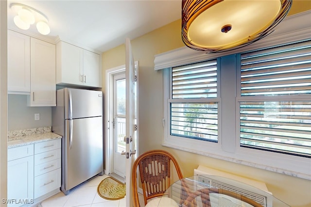 kitchen with light tile patterned floors, light stone counters, freestanding refrigerator, and white cabinets