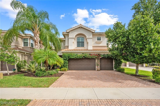 mediterranean / spanish-style home featuring a garage, decorative driveway, a tile roof, and stucco siding